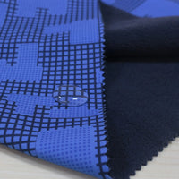 A close-up of Longon Craft Waterproof Polar Fleece Fabric shows its blue and black pattern repelling water, with a soft solid black reverse side. This 4-way stretch polyester fabric is ideal for durable, comfy outdoor gear by the yard.