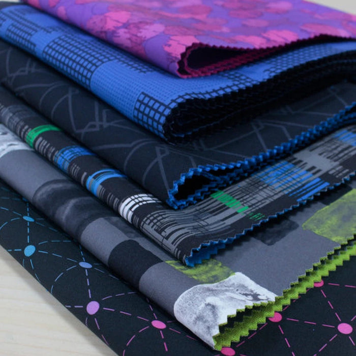 A stack of Longon Craft Waterproof Polar Fleece Fabric by the yard, featuring 4-way stretch polyester with geometric and abstract blue, purple, green, and black patterns, is displayed on a light surface.
