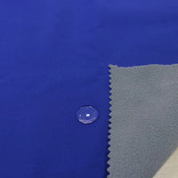 A close-up of Longon Craft's Waterproof Polar Fleece Fabric By The Yard shows a water droplet beading on its blue, 4-way stretch polyester surface, with a corner flipped to reveal its soft gray underside.