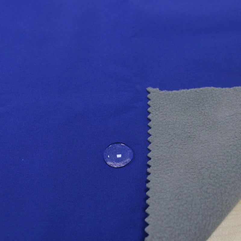 A close-up of Longon Craft's Waterproof Polar Fleece Fabric By The Yard shows a water droplet beading on its blue, 4-way stretch polyester surface, with a corner flipped to reveal its soft gray underside.